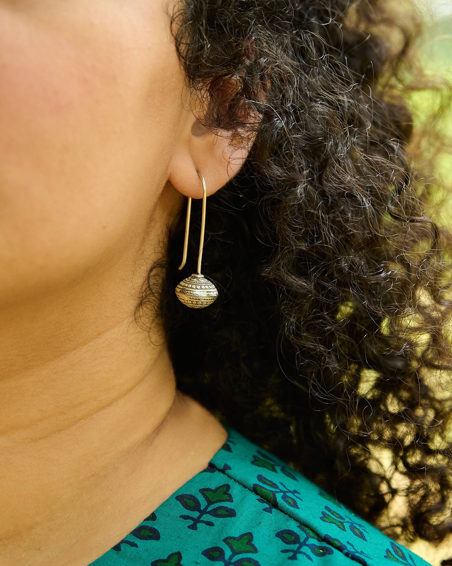 Close up of a ball drop silver earring with a simple hand built wire hanging.