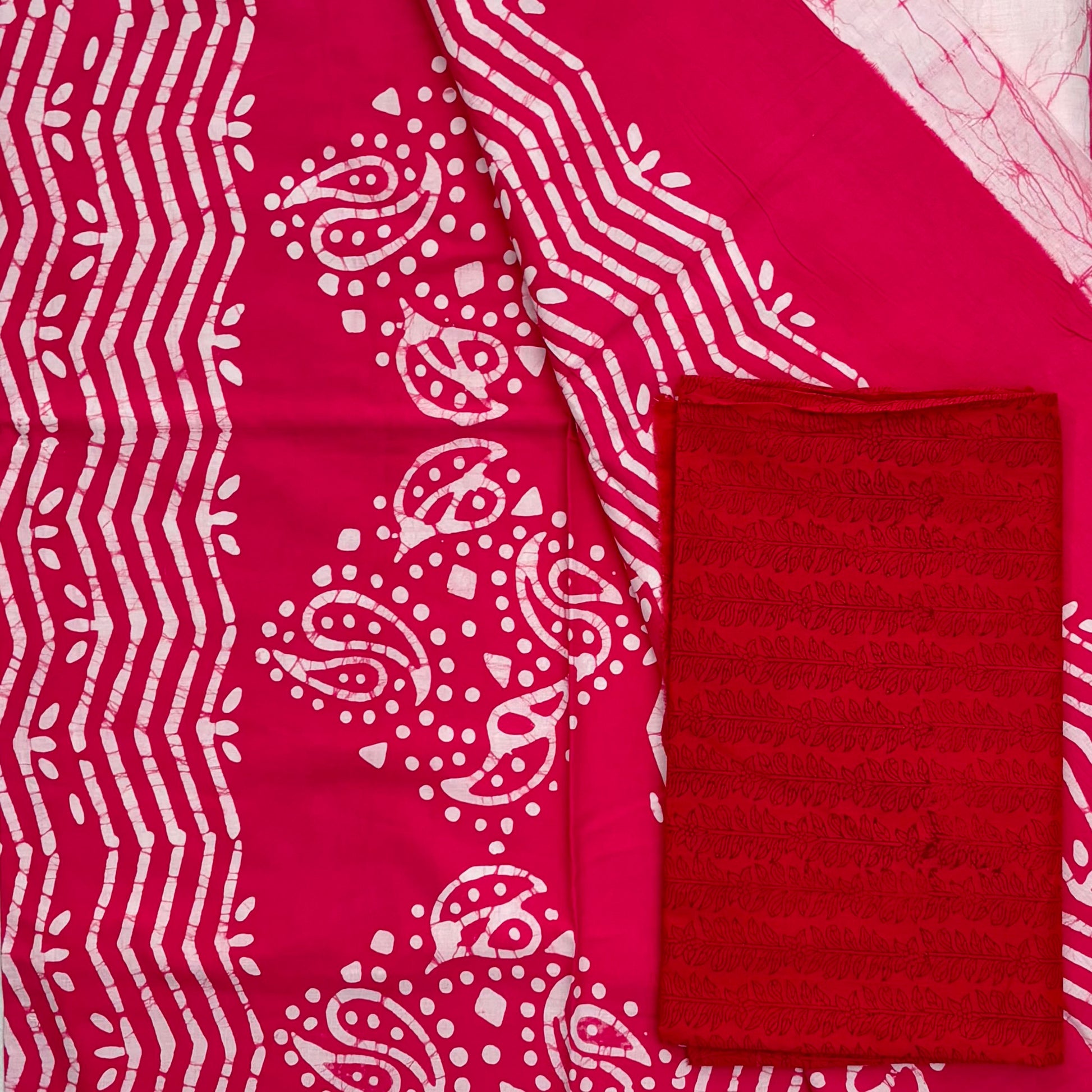 Cotton saree with light pink body with thread like batik patterns all over and a dark pink pallu with batik design in white and a contrasting red blouse material.