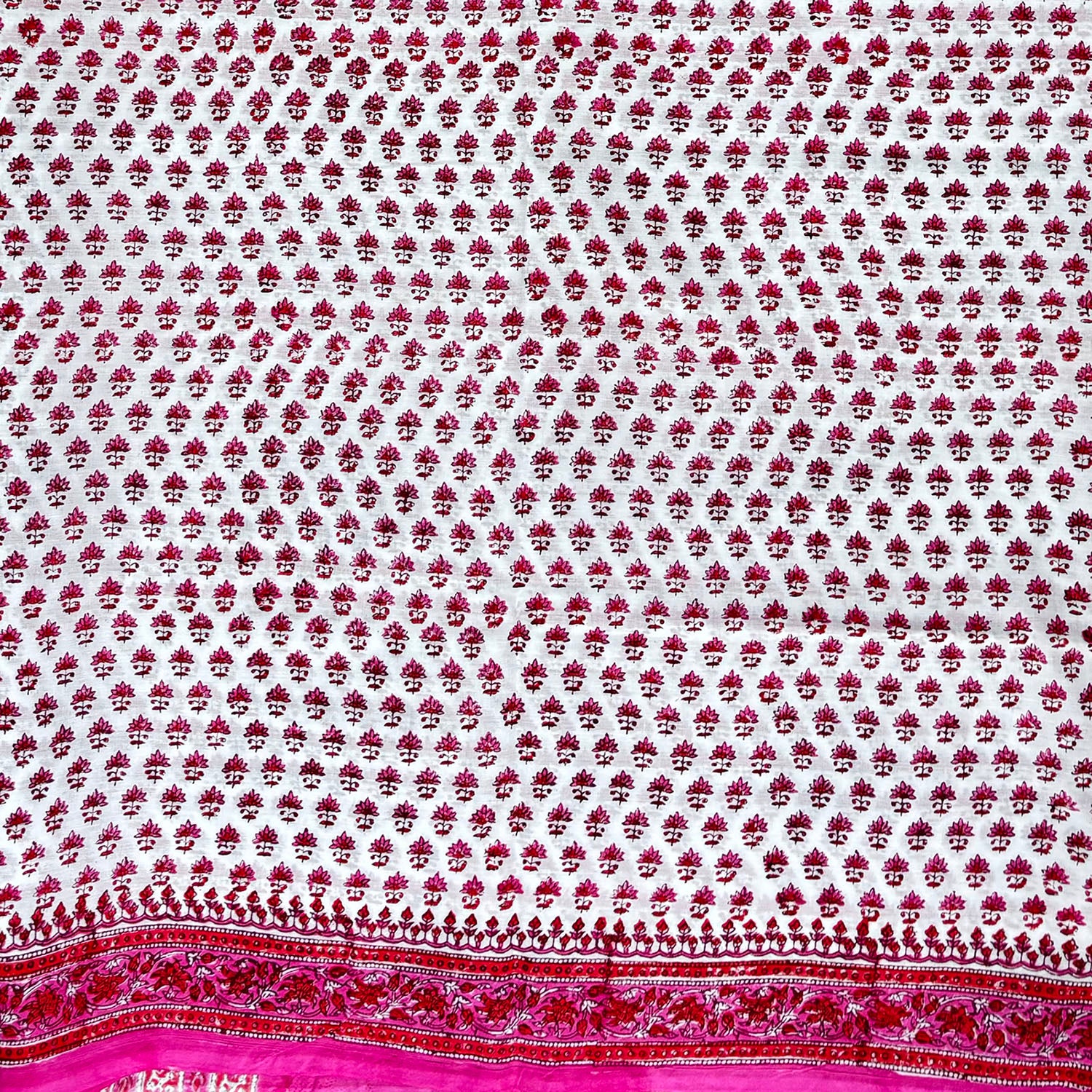 Close up of cotton blockprinted saree with white base and pink and red print.