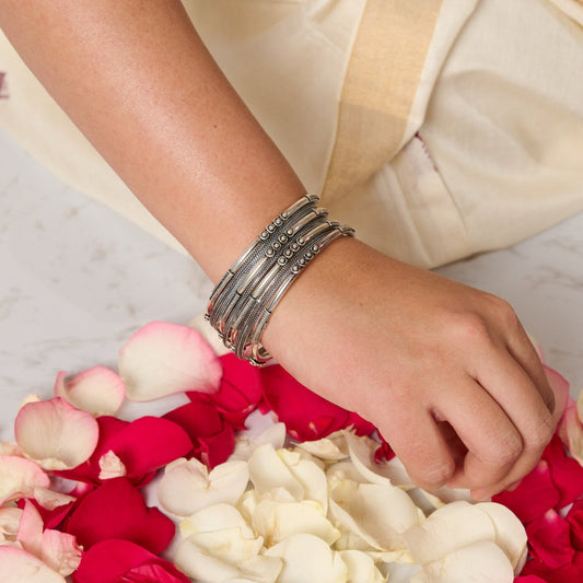 Woman wearing a mixed bangle set in silver making rangoli with rose petals.