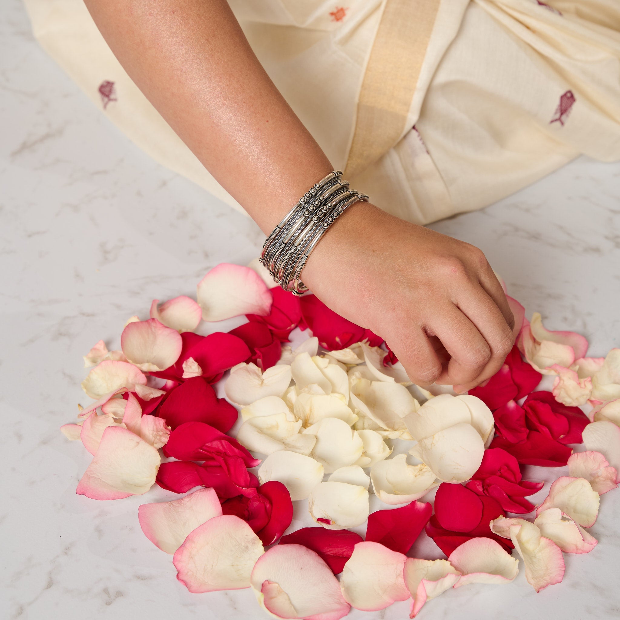 Woman wearing a mixed bangle set in silver making rangoli with rose petals.