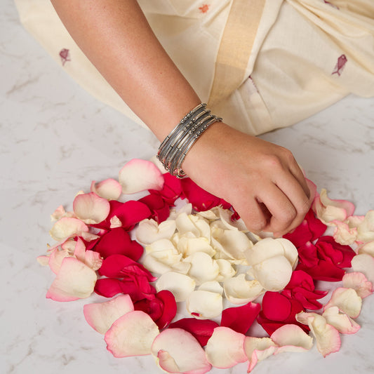 Woman wearing a mixed bangle set in silver making rangoli with rose petals.