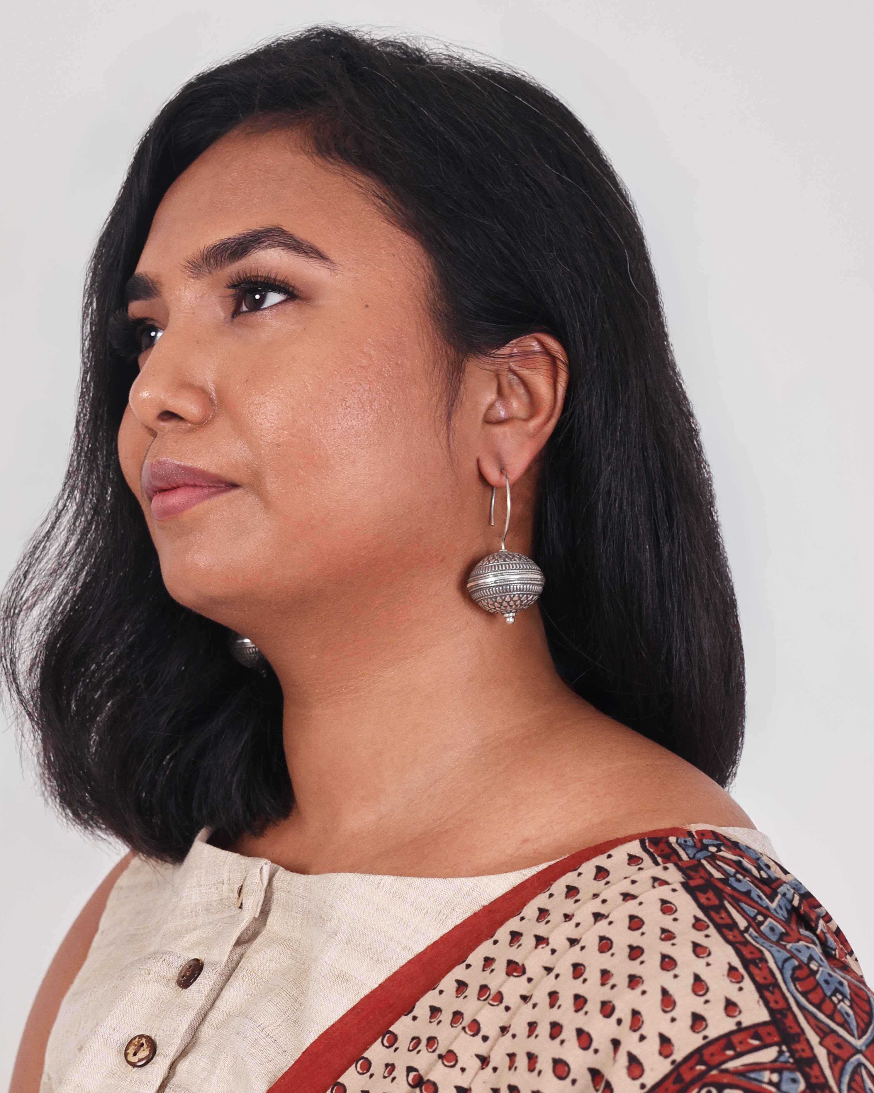 A model is wearing a silver earring with a large engraved ball with a fish hook.