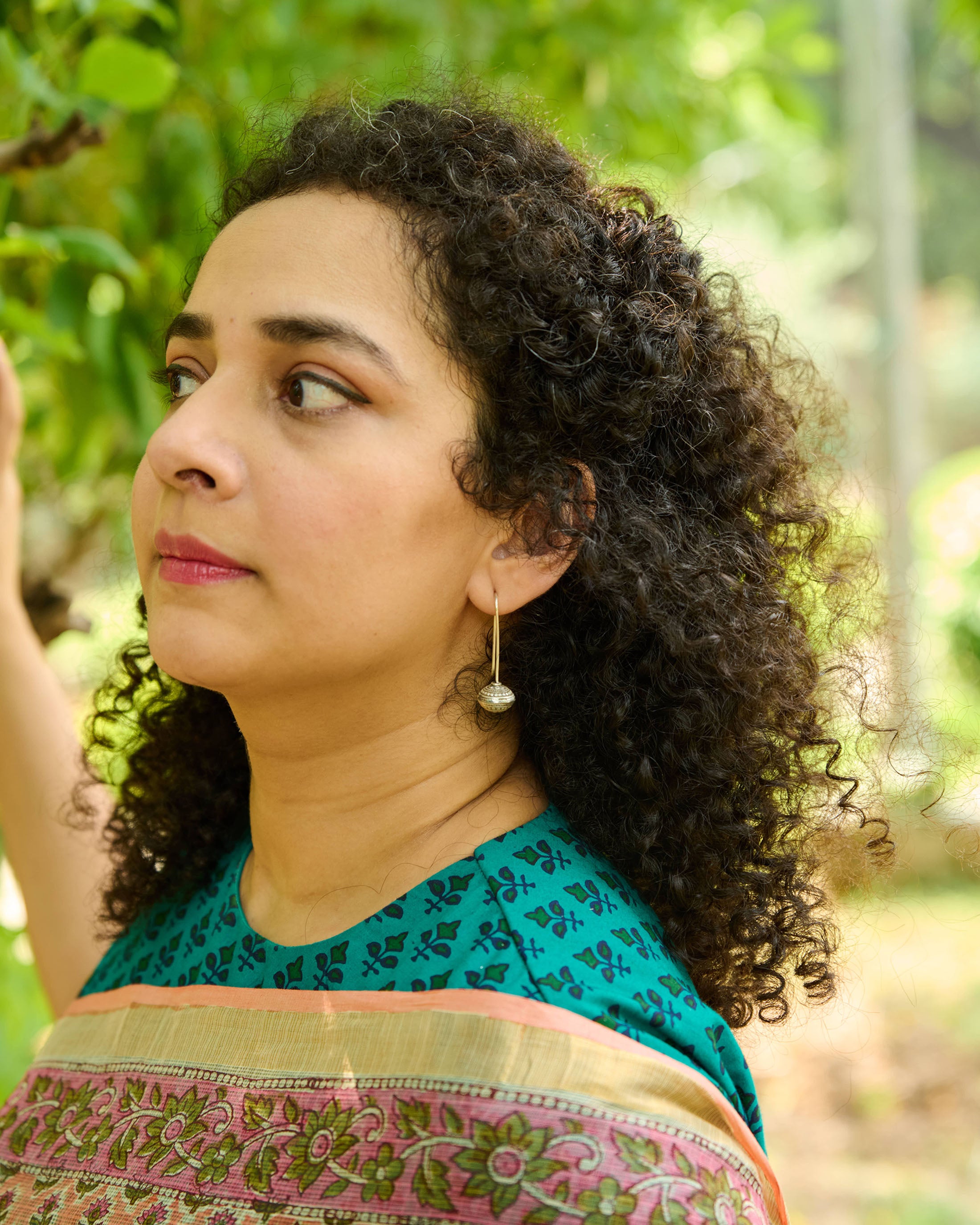 Woman with curly hair in a green blouse and peach floral saree wearing a ball drop silver earring with a simple hand built wire hanging. 