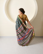 Woman wearing a bhujodi silk saree in grey displaying it's multicolour pallu against a white wall.