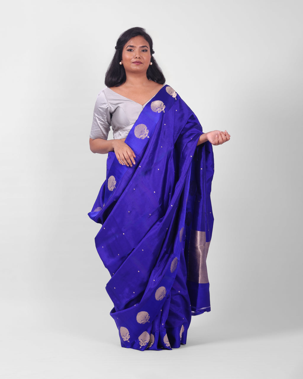 A female model showcasing a royal blue kadwa banarasi silk saree with fine floral motifs all over the saree and wide mashru silk border adorned with more prominent floral motifs.

