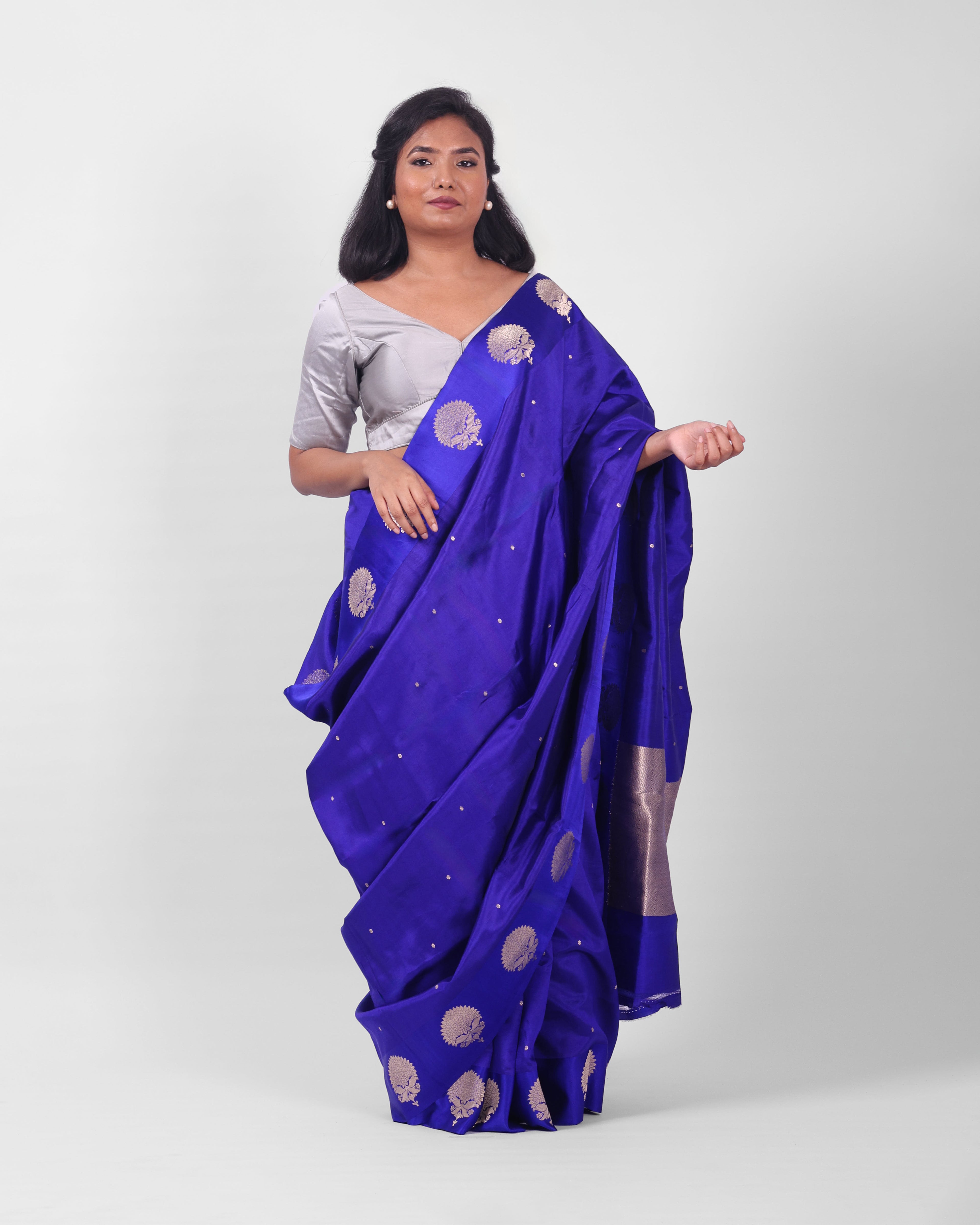 A female model showcasing a royal blue kadwa banarasi silk saree with fine floral motifs all over the saree and wide mashru silk border adorned with more prominent floral motifs.
