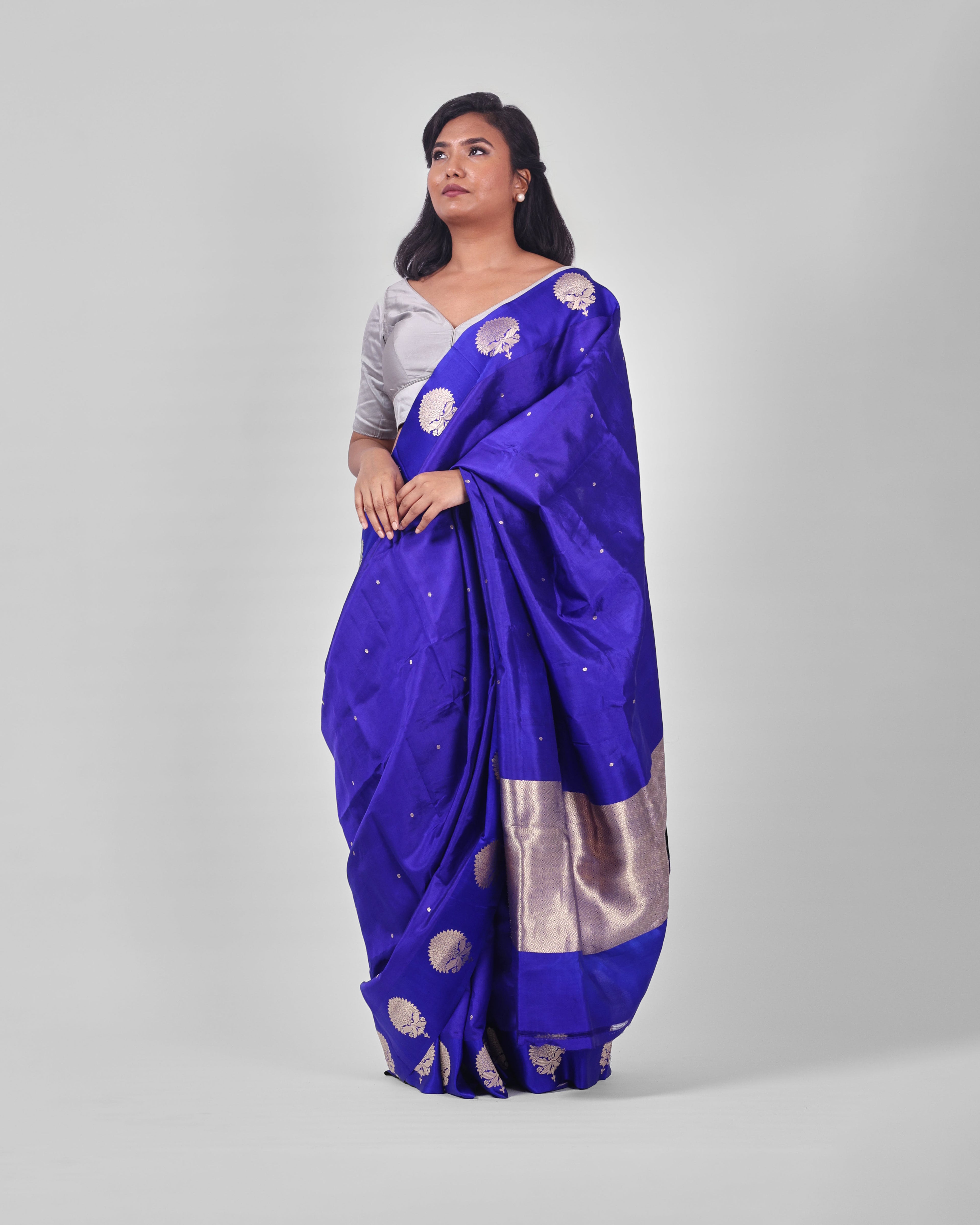 A female model showcasing a royal blue kadwa banarasi silk saree with fine floral motifs all over the saree and wide mashru silk border adorned with more prominent floral motifs.
