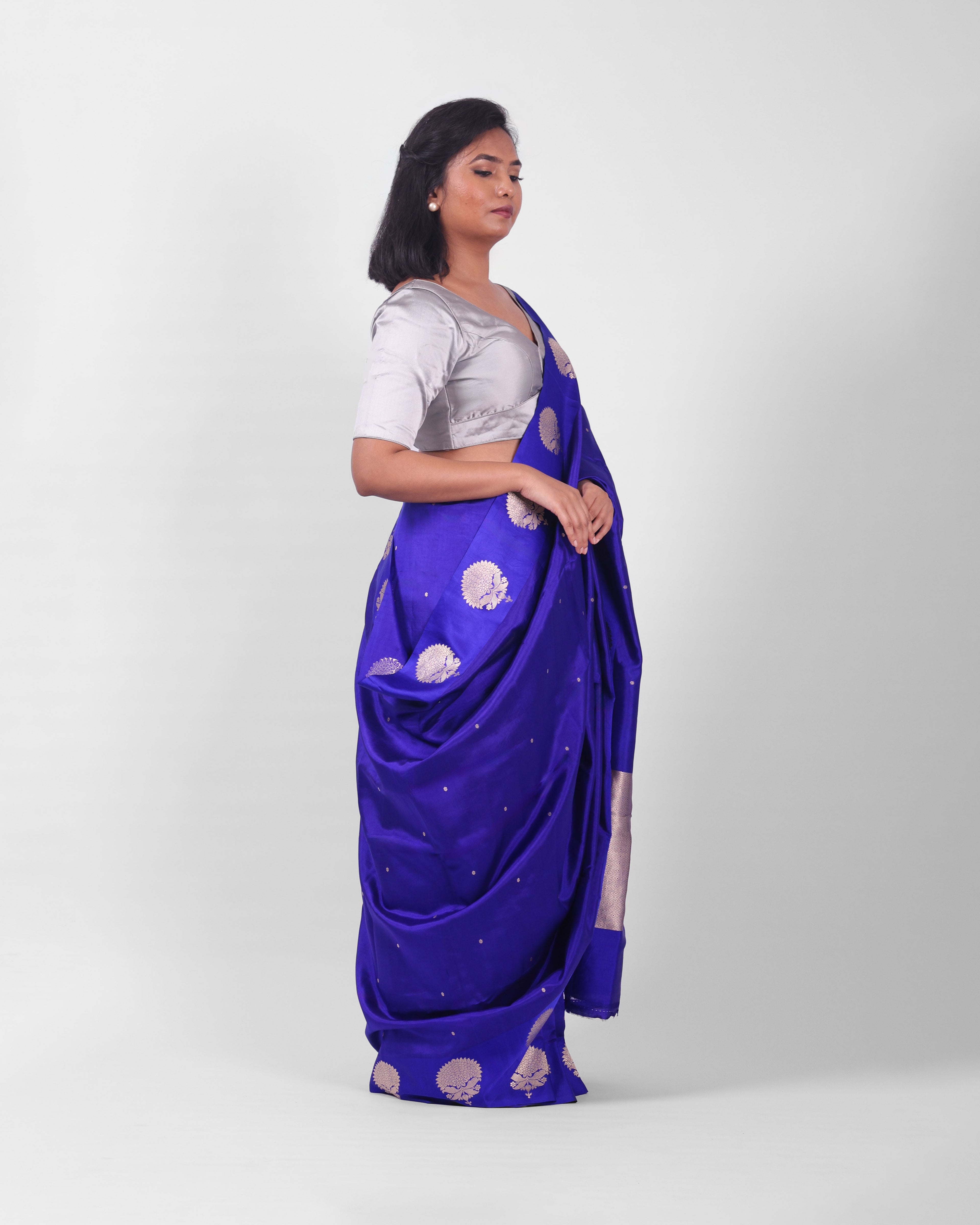 A female model showcasing a royal blue kadwa banarasi silk saree with fine floral motifs all over the saree and wide mashru silk border adorned with more prominent floral motifs.
