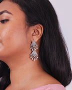 Close up of a Model is wearing a silver earring with kalka inspired forms with ghungroo at the end. 