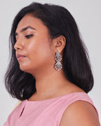 Model is wearing a silver earring with kalka inspired forms with ghungroo at the end. 