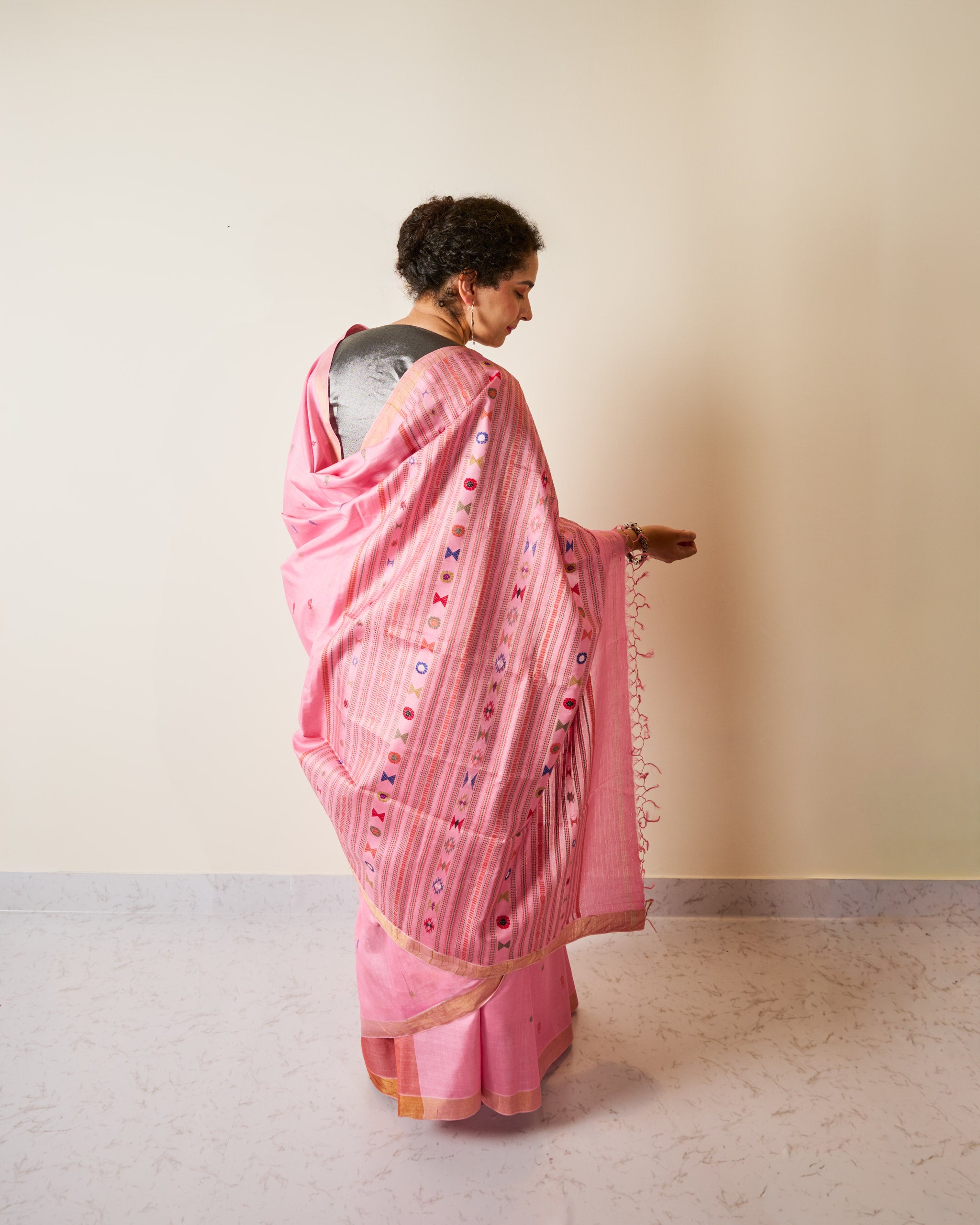 Woman wearing a pink kosa silk saree standing against a plain wall.