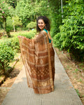 Woman wearing a brown dabu block print kota silk saree playfully strolling down a pavement in a park. 