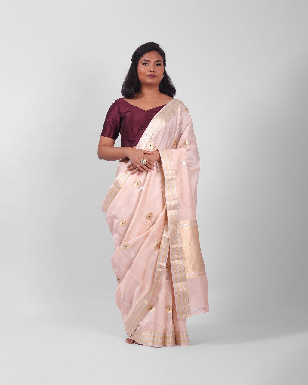 A woman modeling a blush pink banarasi kadwa saree with golden and silver zari borders and a zari minakari marigold motifs all over the saree, and an ornate pallu. 

