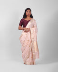 A woman modeling a blush pink banarasi kadwa saree with golden and silver zari borders and a zari minakari marigold motifs all over the saree, and an ornate pallu. 

