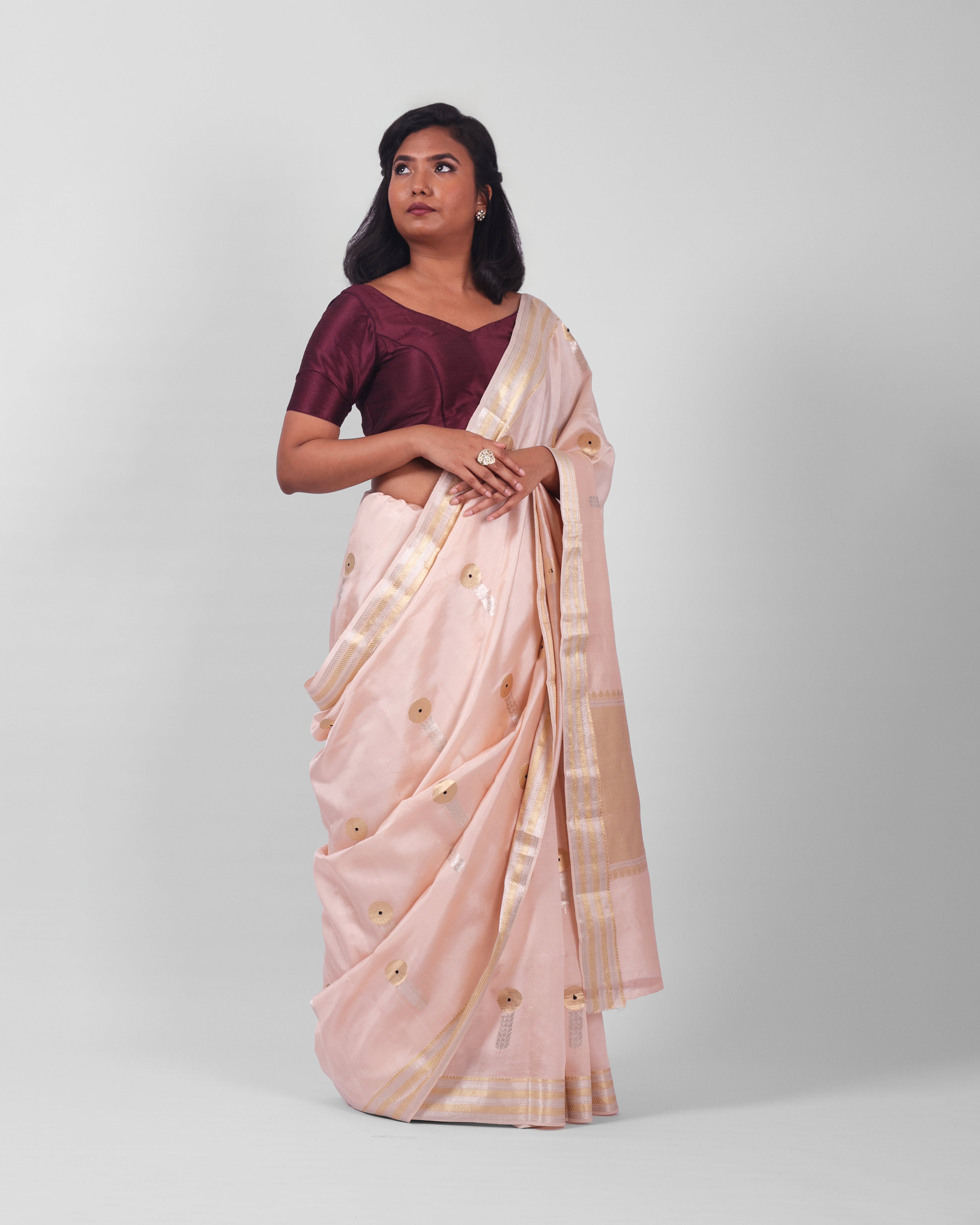 A woman modeling a blush pink banarasi kadwa saree with golden and silver zari borders and a zari minakari marigold motifs all over the saree, and an ornate pallu. 
