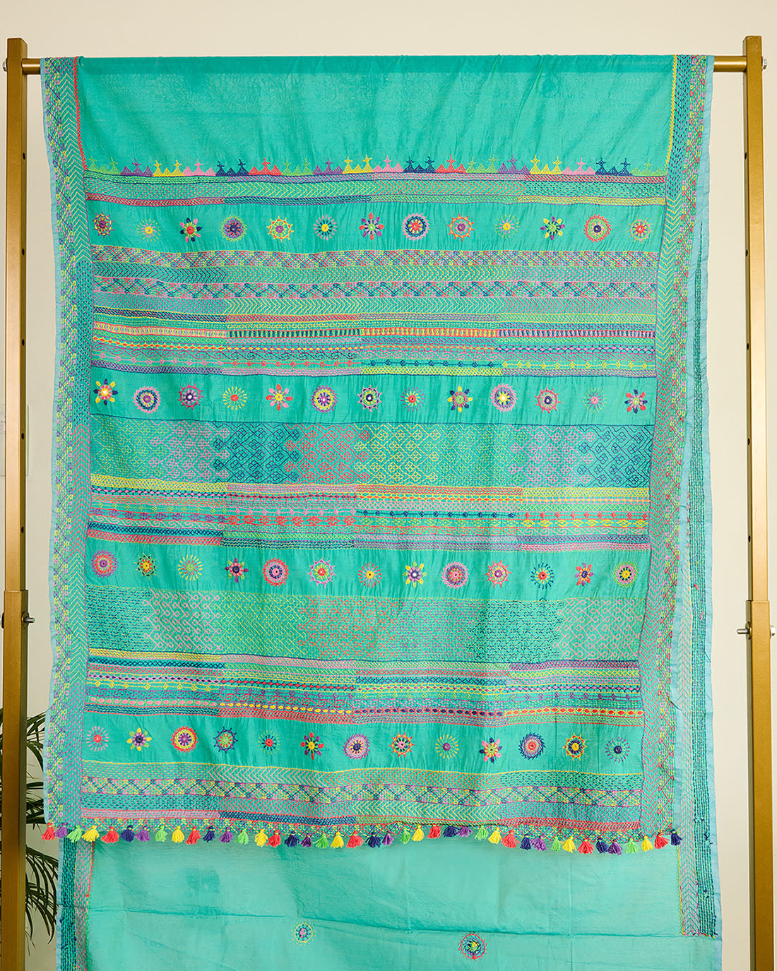 Turquoise chanderi silk cotton saree with colourful Lambani embroidery on the pallu on display on a stand.