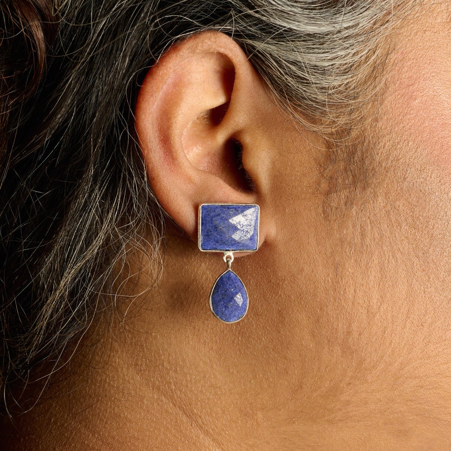 Close-up of an ear wearing a lapis lazuli earring with a teardrop design.

