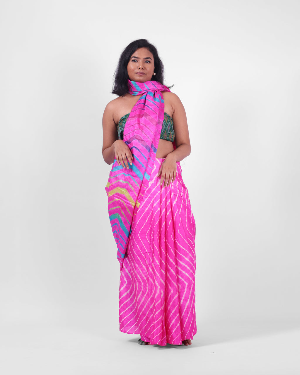 A model is wearing this pink leheriya saree in tussar, the pallu is draped like a stole around her neck. The body of the saree is a pink and white leheriya with a multicolour leheriya on pallu. 