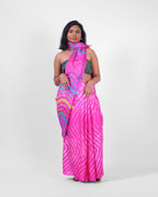 A model is wearing this pink leheriya saree in tussar, the pallu is draped like a stole around her neck. The body of the saree is a pink and white leheriya with a multicolour leheriya on pallu. 
