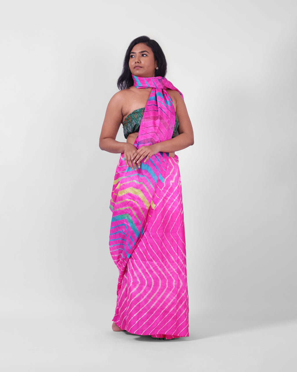 A model is wearing this pink leheriya saree in tussar, the pallu is draped like a stole around her neck. The body of the saree is a pink and white leheriya with a multicolour leheriya on pallu. 