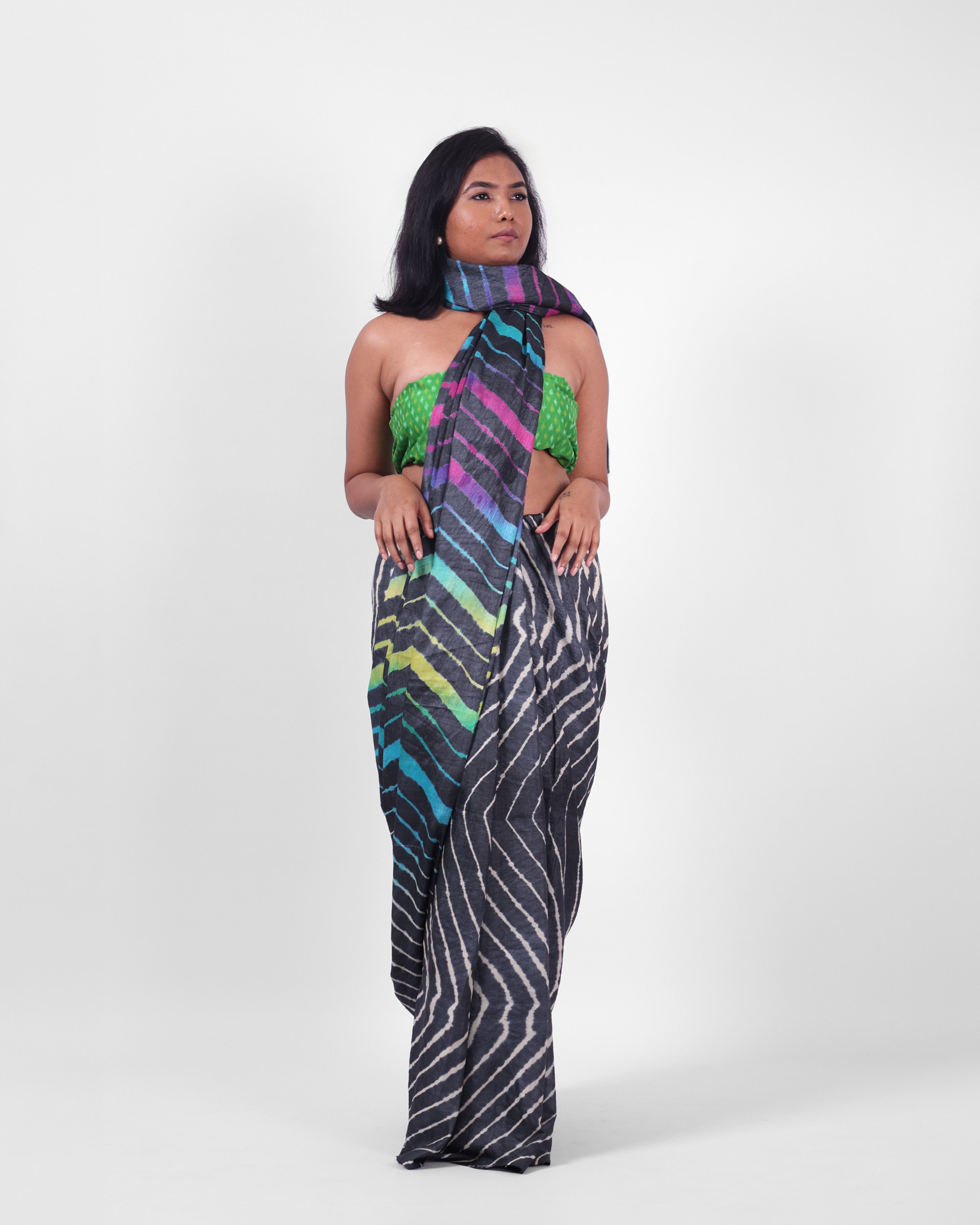 A model is wearing this black leheriya saree in tussar, the pallu is draped like a stole around her neck. The body of the saree is a pink and white leheriya with a multicolour leheriya on pallu. 