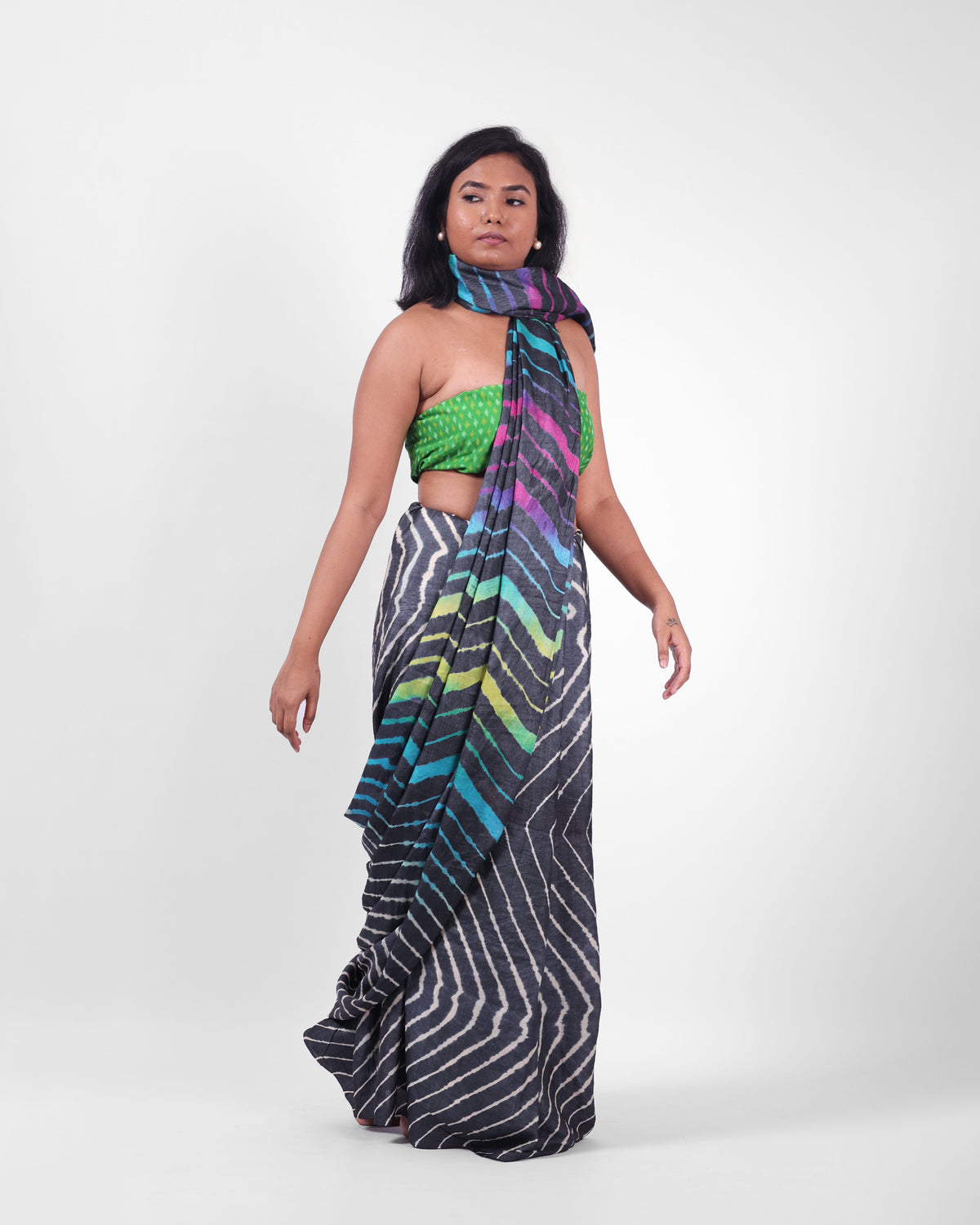 A model is wearing this black leheriya saree in tussar, the pallu is draped like a stole around her neck. The body of the saree is a pink and white leheriya with a multicolour leheriya on pallu. 