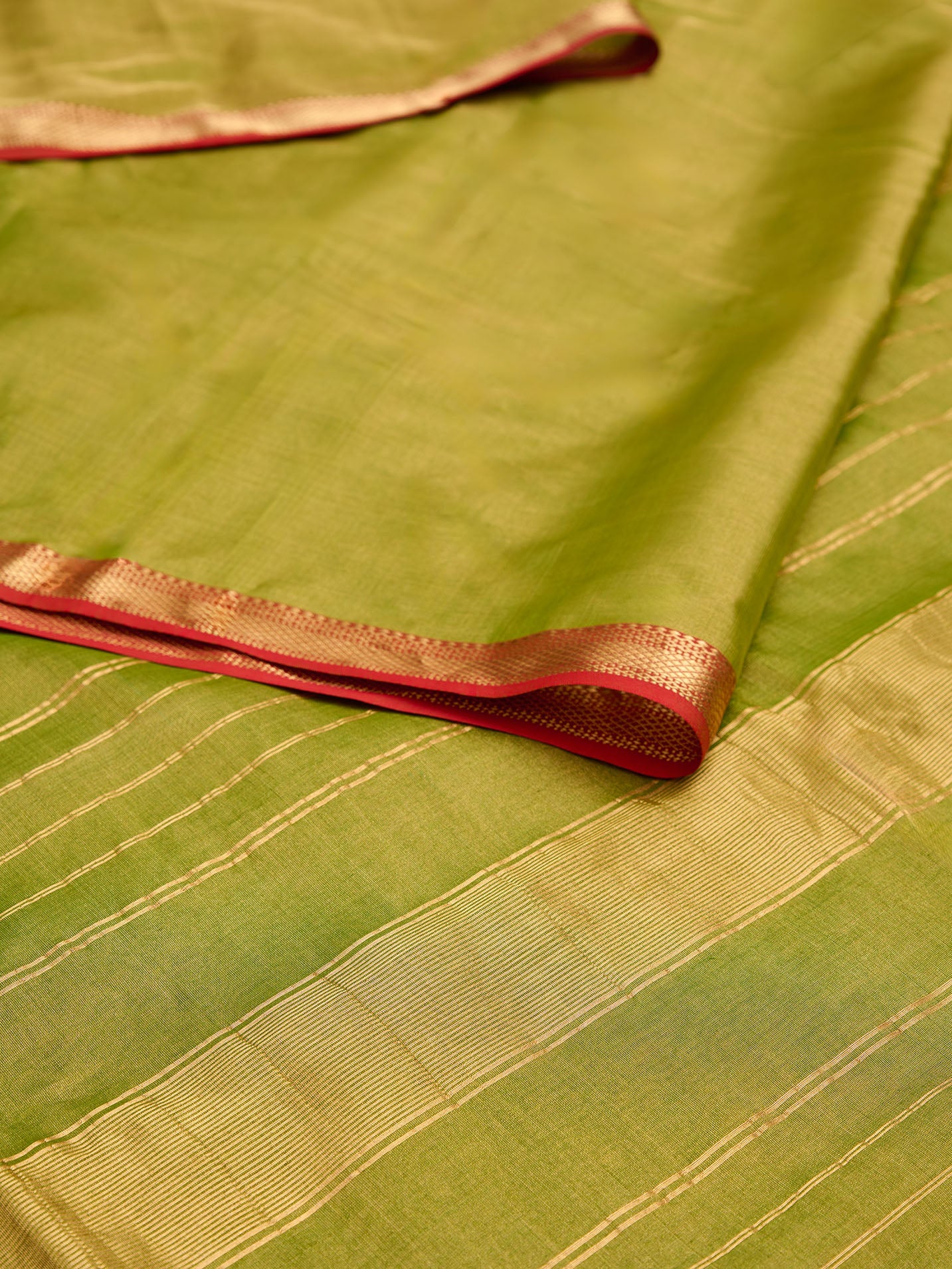 A maheshwari tissue saree in dual tone of light green and gold on display on a flat surface.