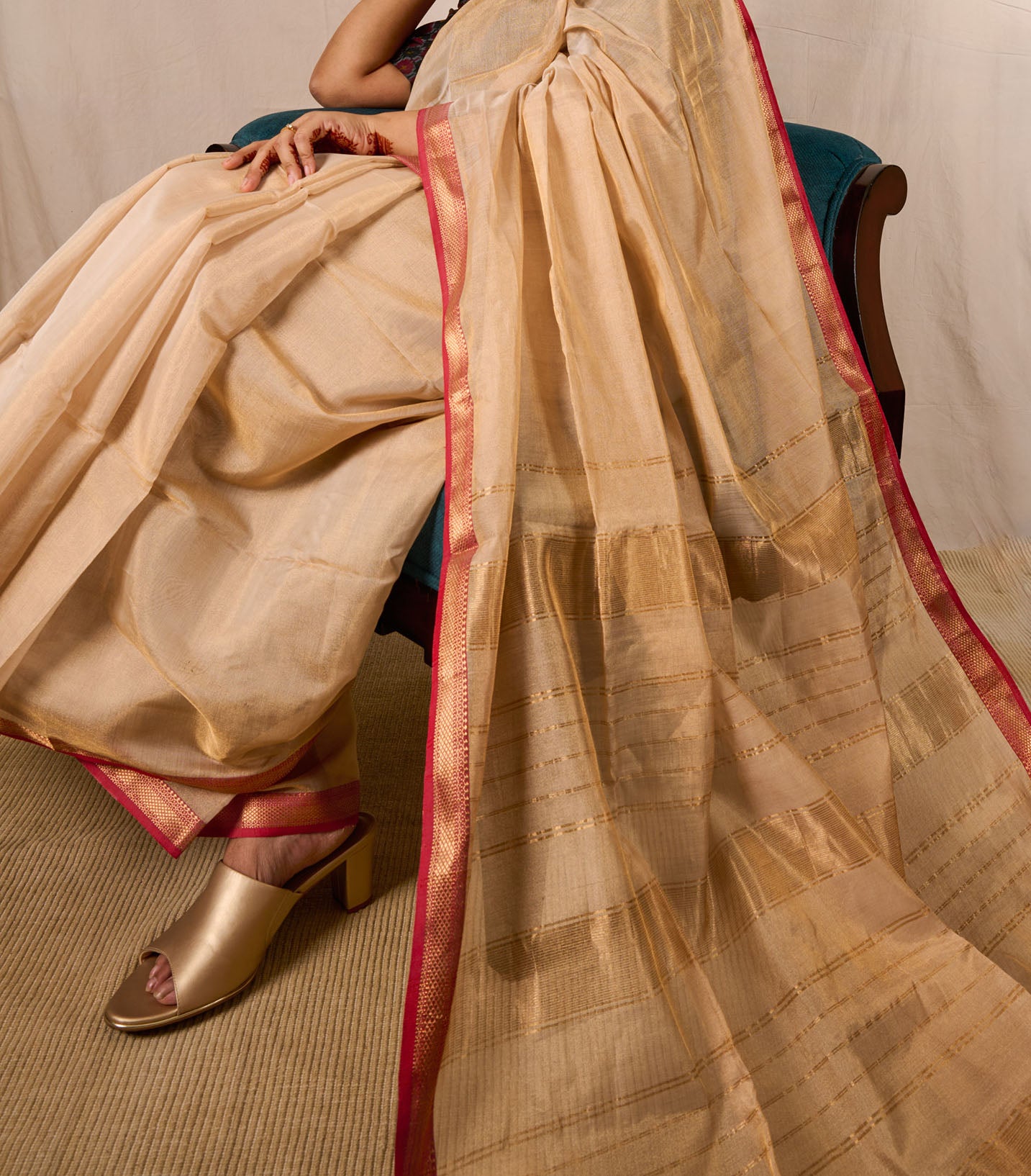 Model seated on an accent chair in a maheshwari tissue saree with the pallu laid out beautifully