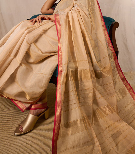 Model seated on an accent chair in a maheshwari tissue saree with the pallu laid out beautifully