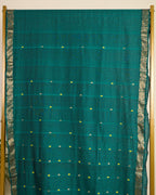 Assam cotton saree in teal green colour with traditional motifs and ornate zari border on display.
