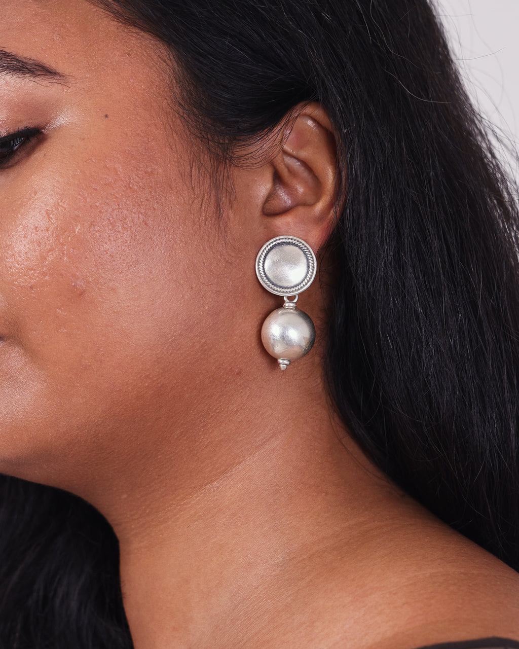 Model wearing a classic and clean design of silver ball drop earrings on her left ear. 
