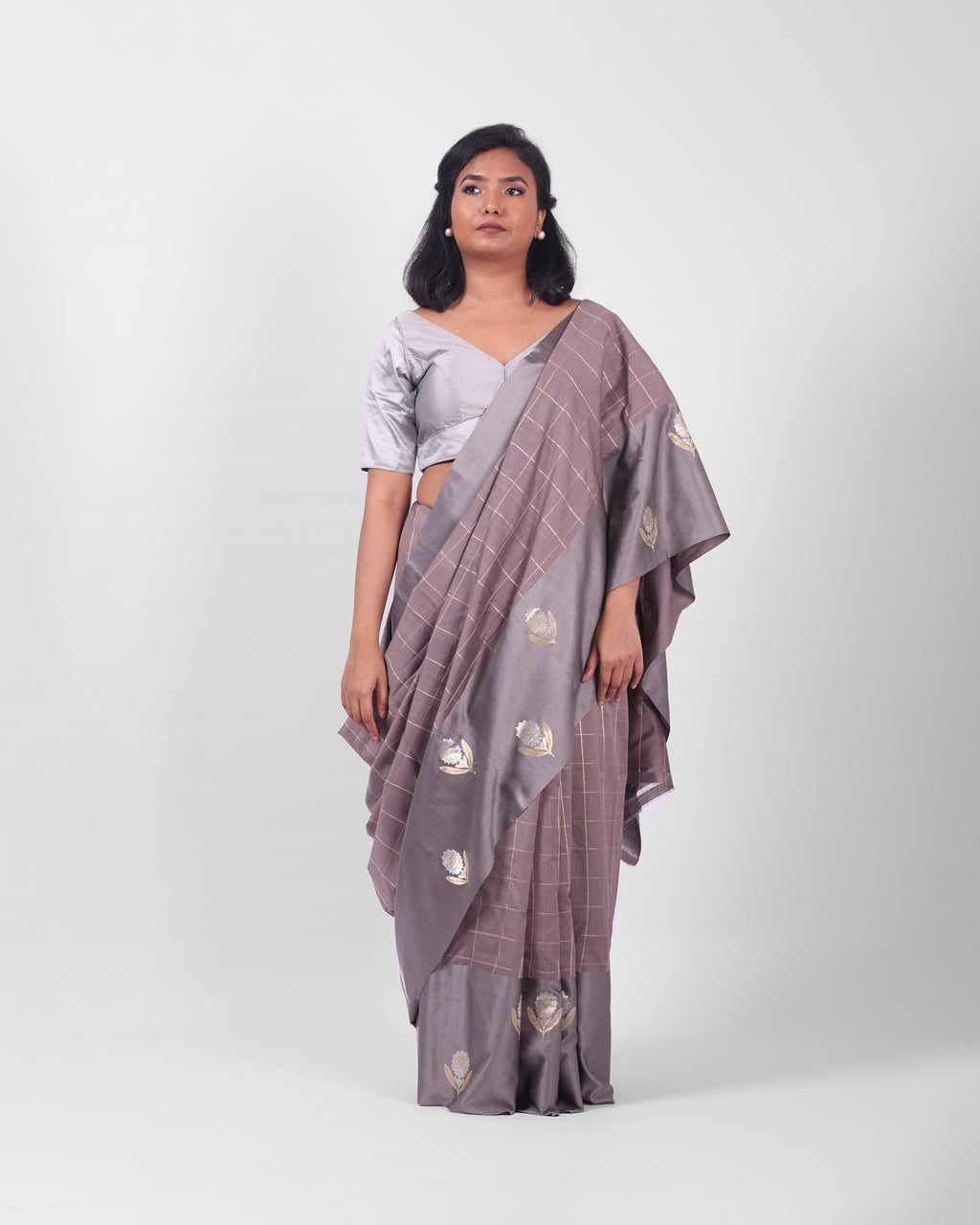 A woman modeling a lavendar gray banarasi kadwa saree with a subtle check pattern and a wide mashru silk border with floral kadwa motifs.
