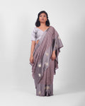 A woman modeling a lavendar gray banarasi kadwa saree with a subtle check pattern and a wide mashru silk border with floral kadwa motifs.
