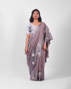 A woman modeling a lavendar gray banarasi kadwa saree with a subtle check pattern and a wide mashru silk border with floral kadwa motifs.
