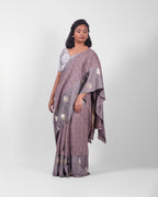 A woman modeling a lavendar gray banarasi kadwa saree with a subtle check pattern and a wide mashru silk border with floral kadwa motifs.
