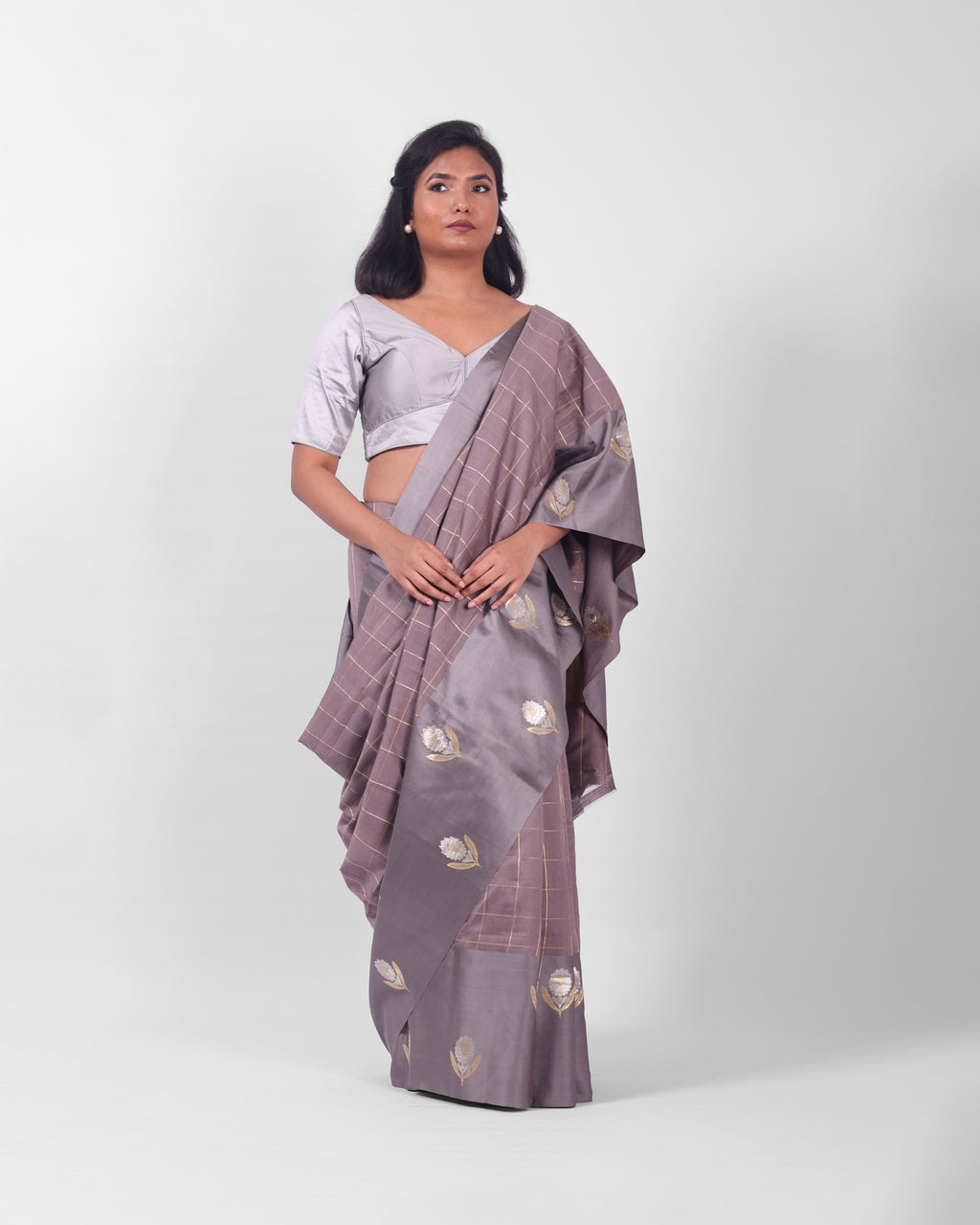 A woman modeling a lavendar gray banarasi kadwa saree with a subtle check pattern and a wide mashru silk border with floral kadwa motifs.
