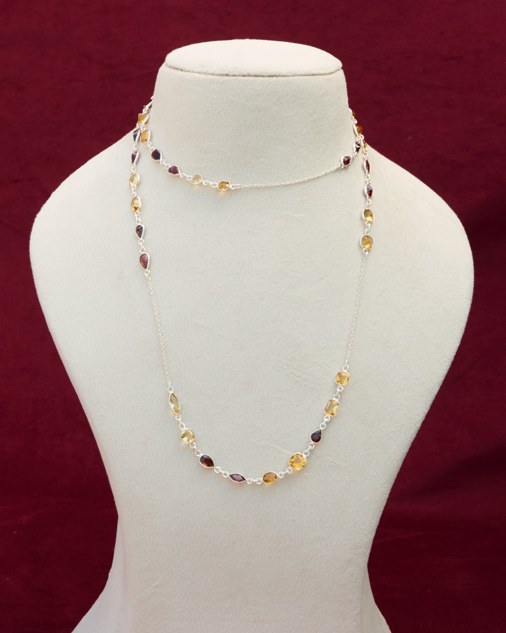 A long neck chain with faceted citrine and garnet semi precious gemstones set in 92.5 silver layered on a manequin. 