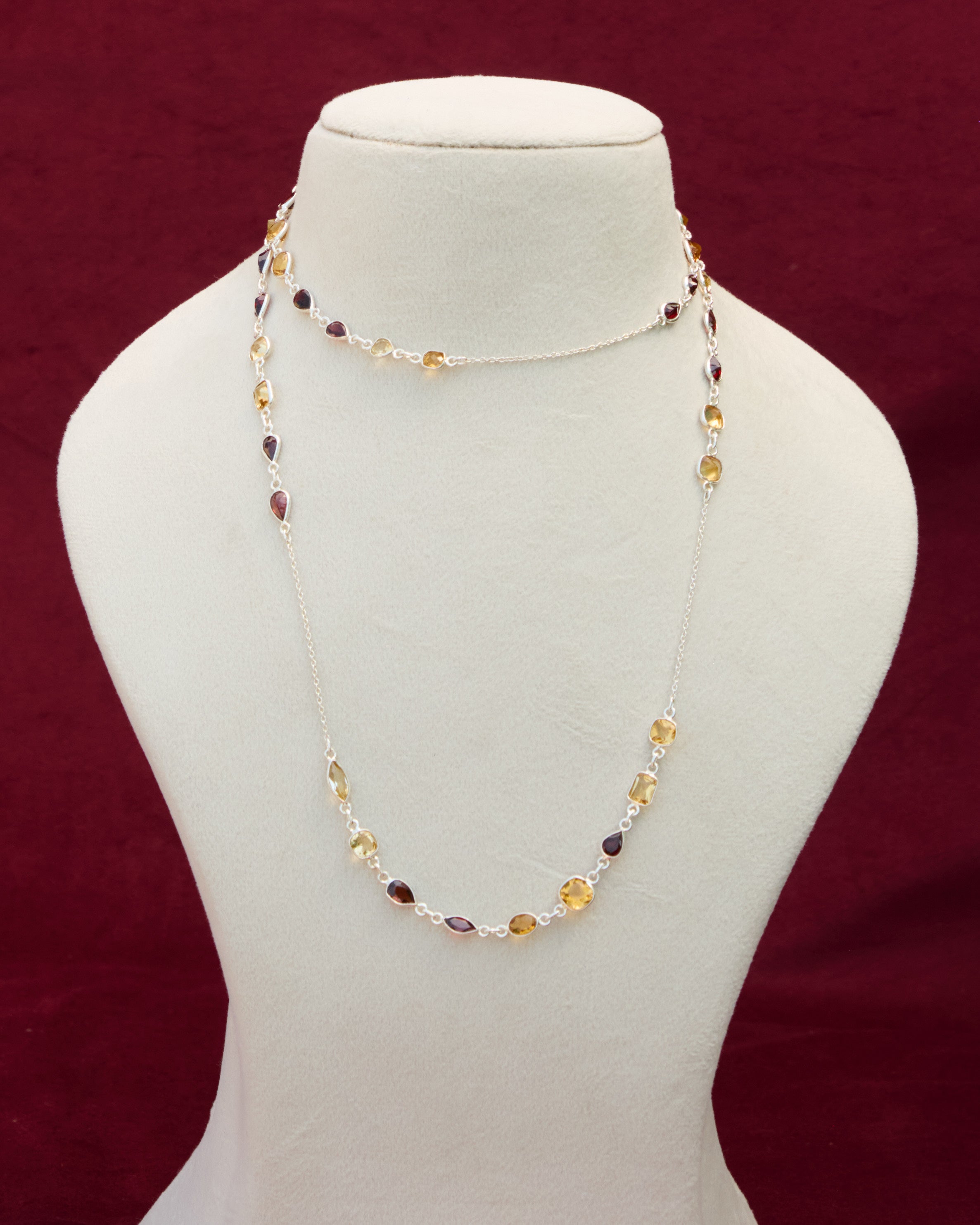 A long neck chain with faceted citrine and garnet semi precious gemstones set in 92.5 silver layered on a manequin. 