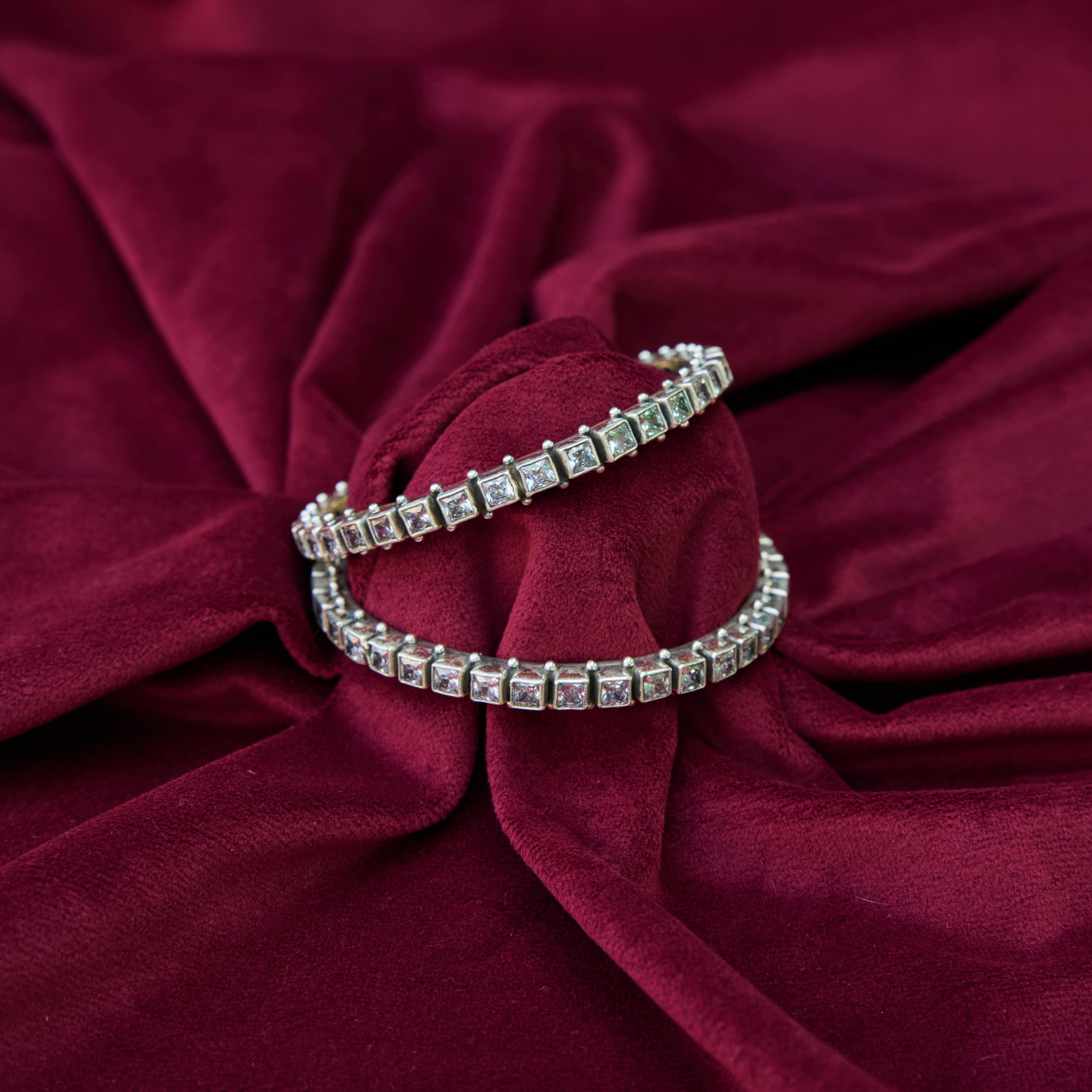 Cut stone design silver bangles with white CZ on red velvet background.