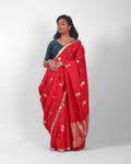 A female model showcasing a bright red silk kadwa banarasi saree with golden and silver zari border and kadwa floral motifs all over the saree. 
