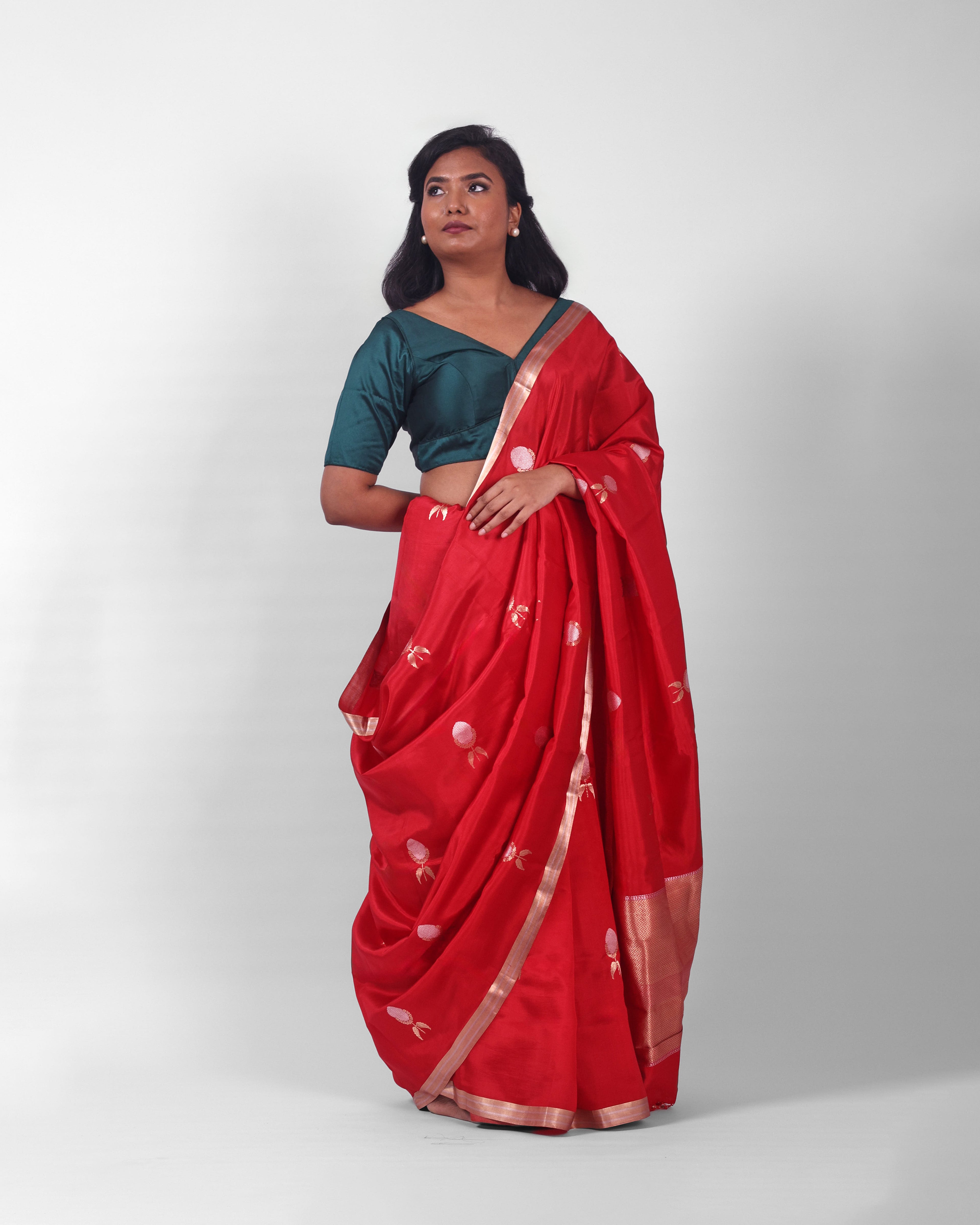 A female model showcasing a bright red silk kadwa banarasi saree with golden and silver zari border and kadwa floral motifs all over the saree. 
