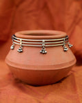 Silver hasli necklace with small hanging ghungroo charms on a terracotta pot against an orange fabric background.