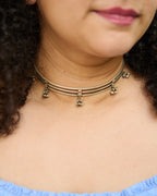 Close up of a model wearing a silver hasli necklace with small hanging ghungroo charms.