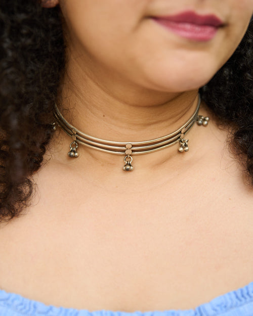 Close up of a model wearing a silver hasli necklace with small hanging ghungroo charms.