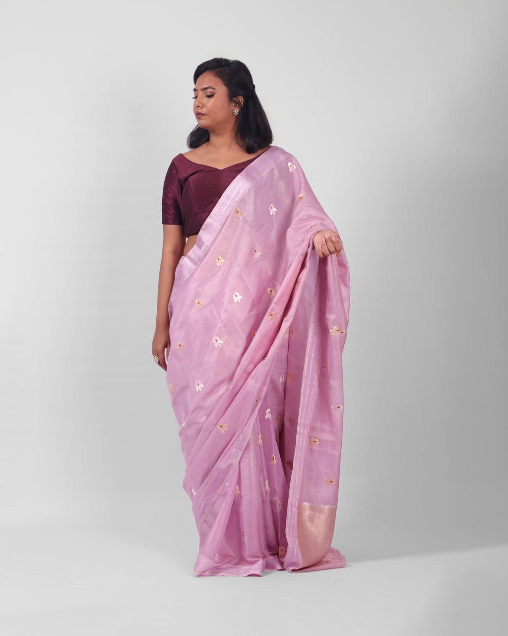 A woman modeling a lilac silk kadwa banarasi saree with small gold floral motifs  with red minakari in the centre all over he saree. 


