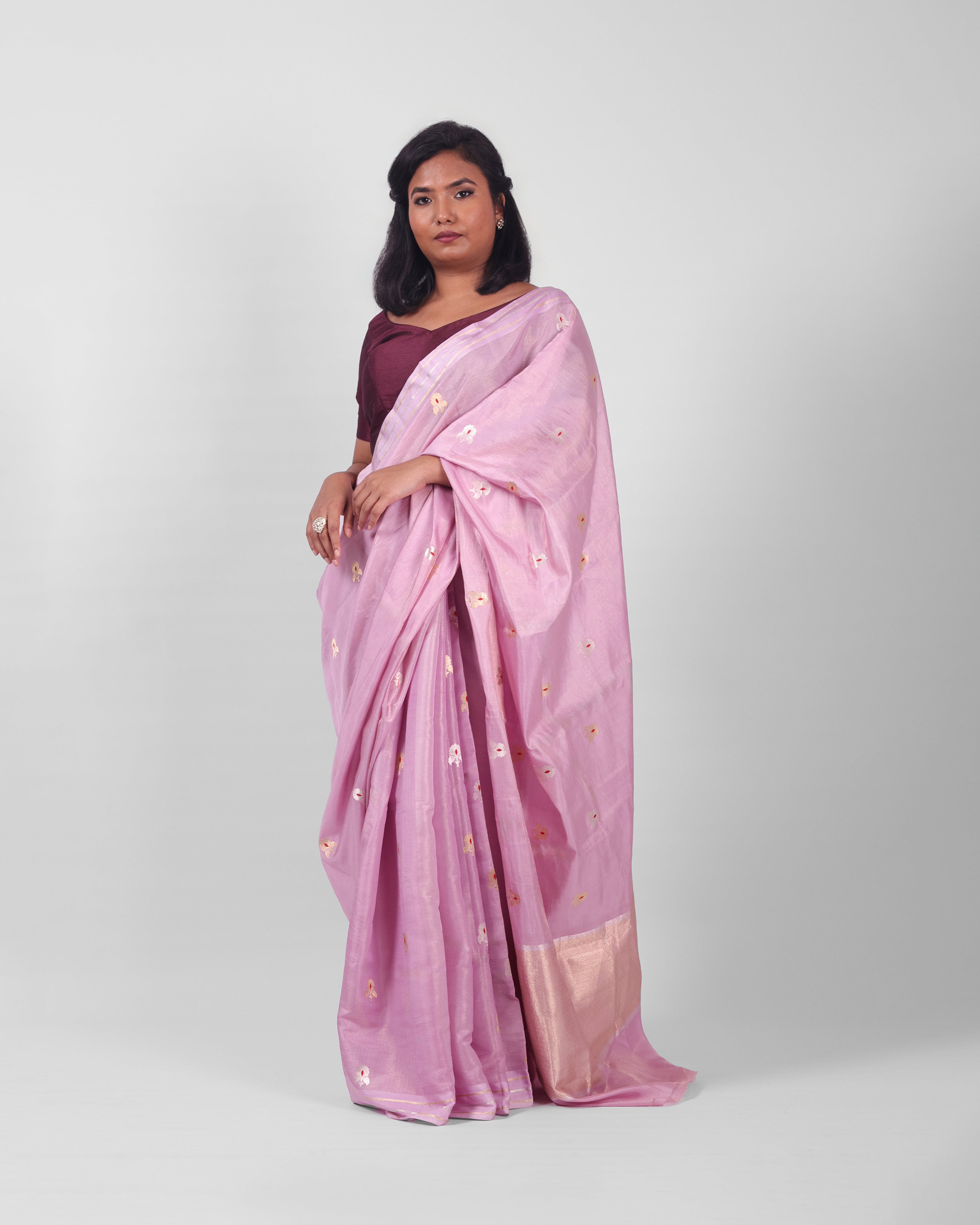 A woman modeling a lilac silk kadwa banarasi saree with small gold floral motifs  with red minakari in the centre all over he saree. 
