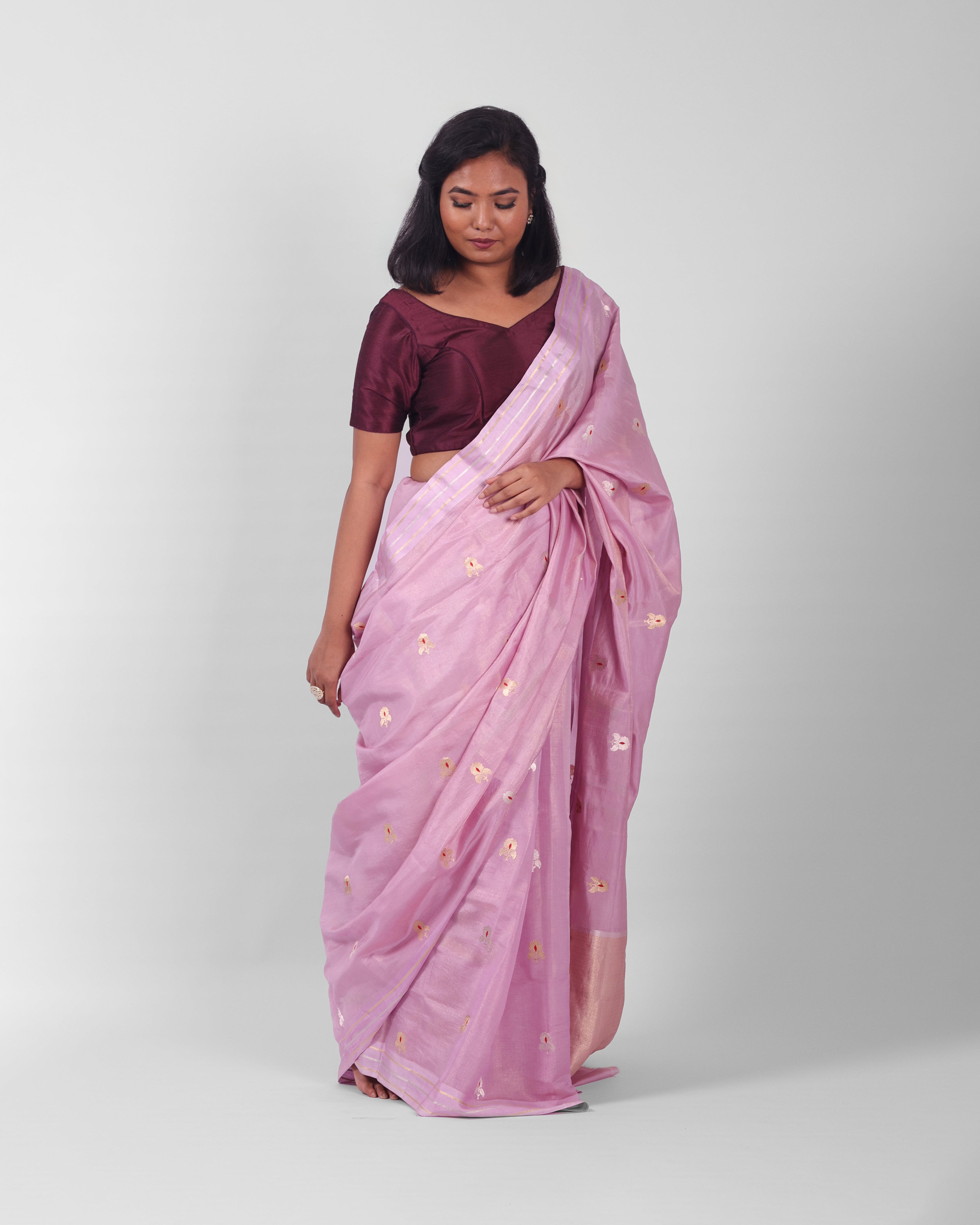 A woman modeling a lilac silk kadwa banarasi saree with small gold floral motifs  with red minakari in the centre all over he saree. 
