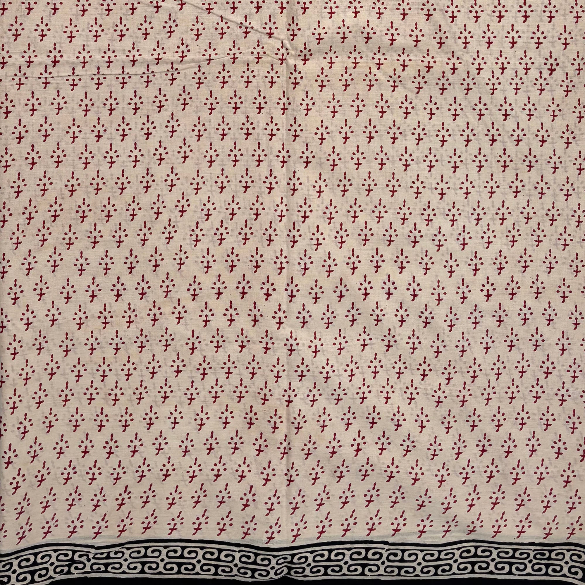 Beige coloured base fabric cotton saree with red booti and black border.