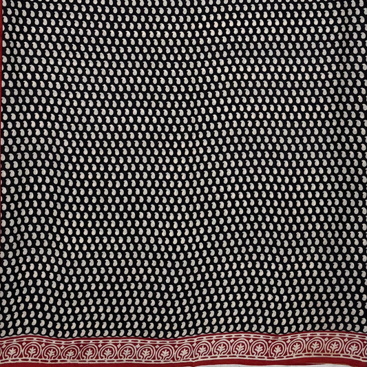 Black base colour cotton block printed saree with small beige paisley booti all over and red border.